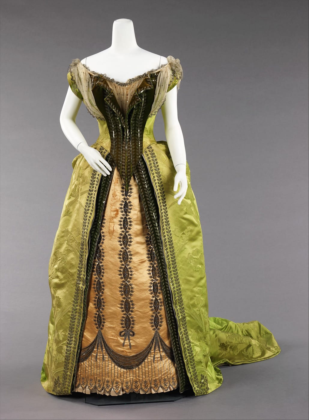 Green silk evening gown on a mannequin, with a gold embroidered panel down the front of the skirt and a train